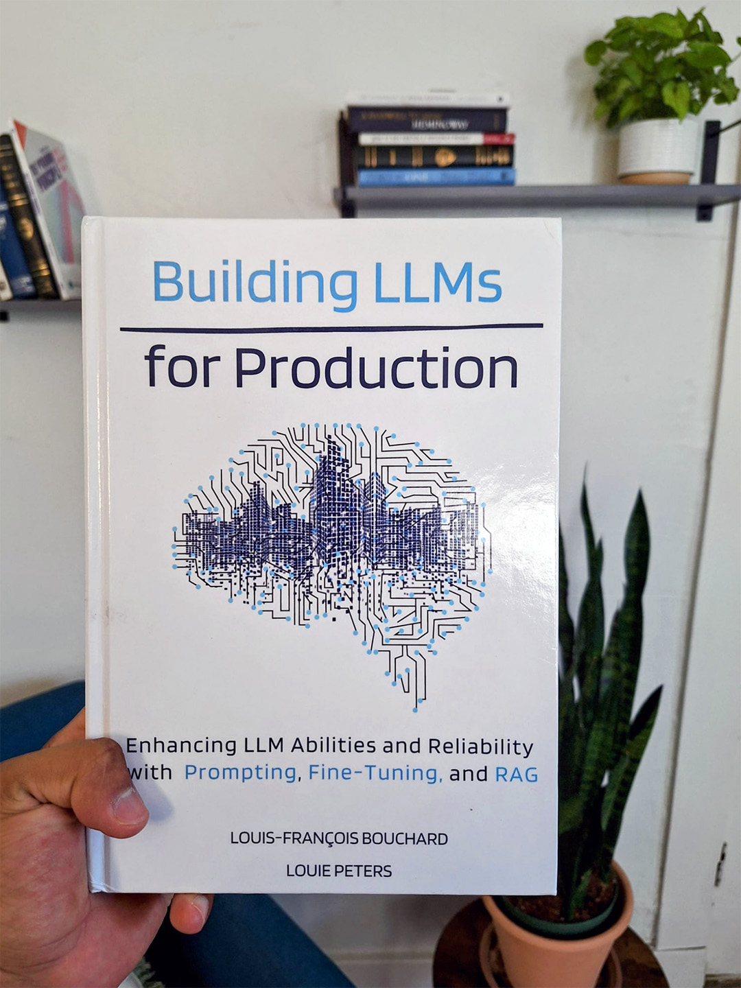 Roberto Iriondo holds the hardcover book edition of "Building LLMs for Production: Enhancing LLM Abilities and Reliability with Prompting, Fine-Tuning, and RAG," authored by Louie Peters and Louis-François Bouchard, and published by Towards AI.